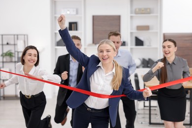 Competition concept. Happy businesswoman crossing red finish line ahead of her colleagues in office