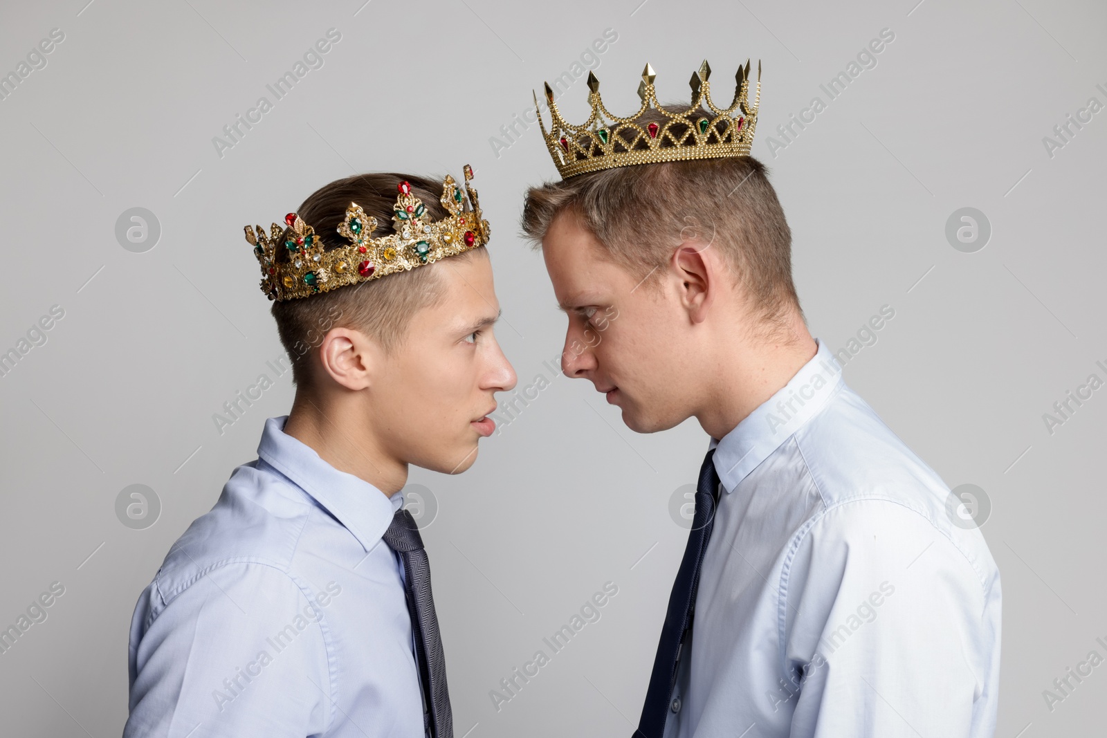 Photo of Business competition. Colleagues in golden crowns looking at each other on grey background