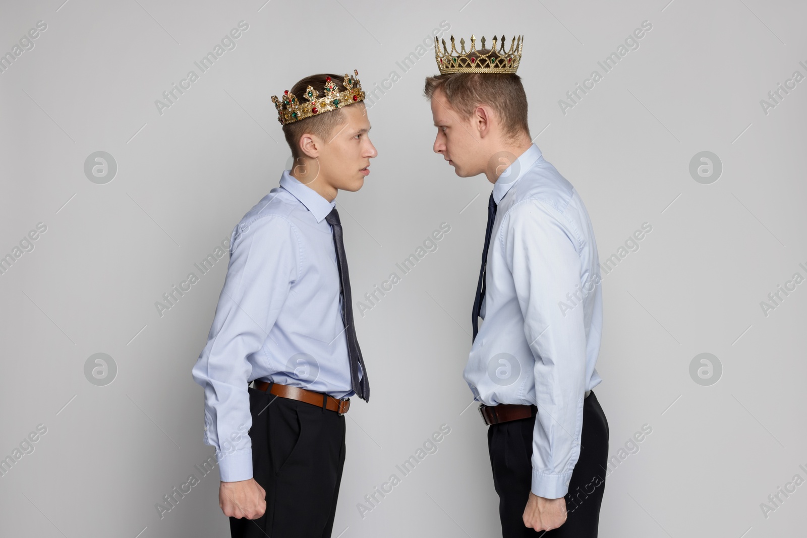 Photo of Business competition. Colleagues in golden crowns looking at each other on grey background