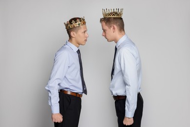 Business competition. Colleagues in golden crowns looking at each other on grey background