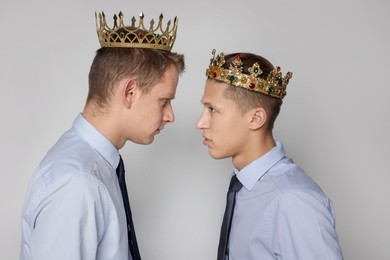 Business competition. Colleagues in golden crowns looking at each other on grey background