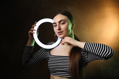 Photo of Beautiful woman with ring lamp on dark background in smoke