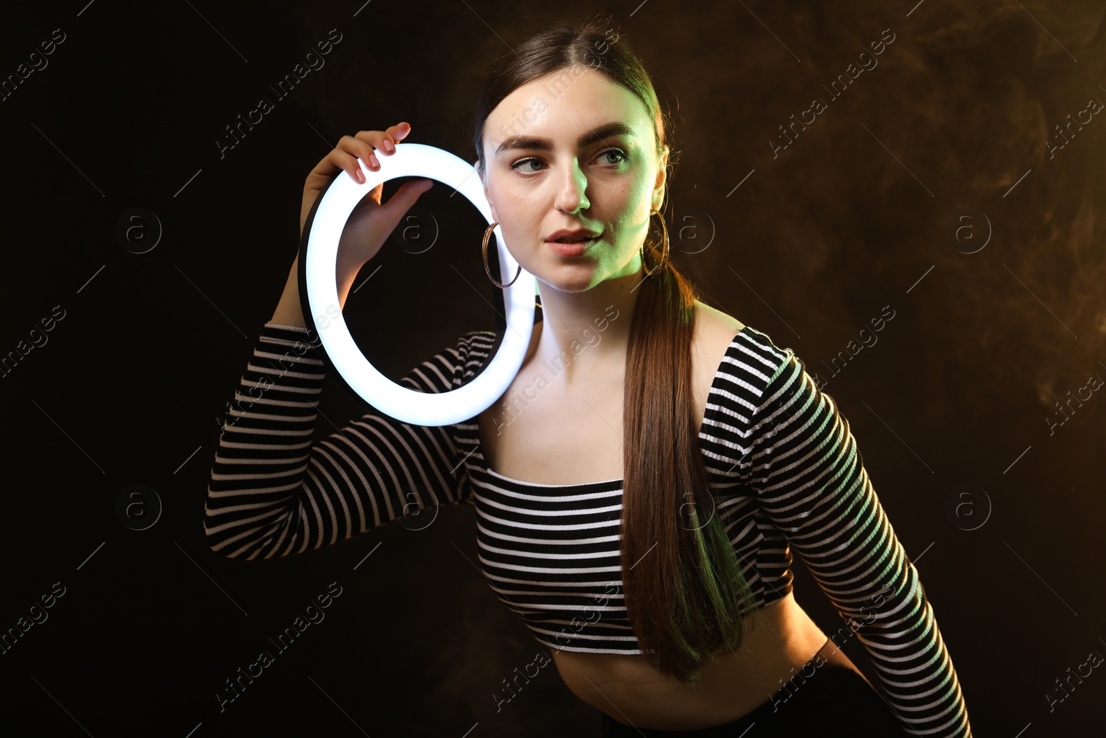 Photo of Beautiful woman with ring lamp on dark background in smoke