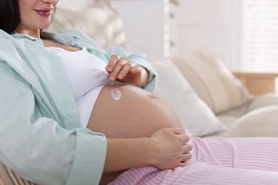 Photo of Pregnant woman applying cream on belly at home, closeup