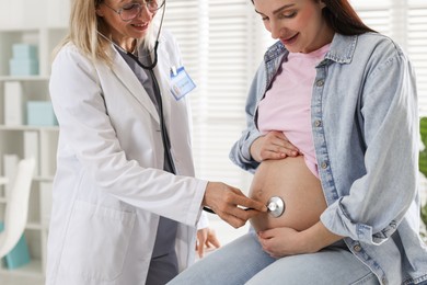 Pregnancy checkup. Doctor with stethoscope listening baby's heartbeat in patient's tummy indoors