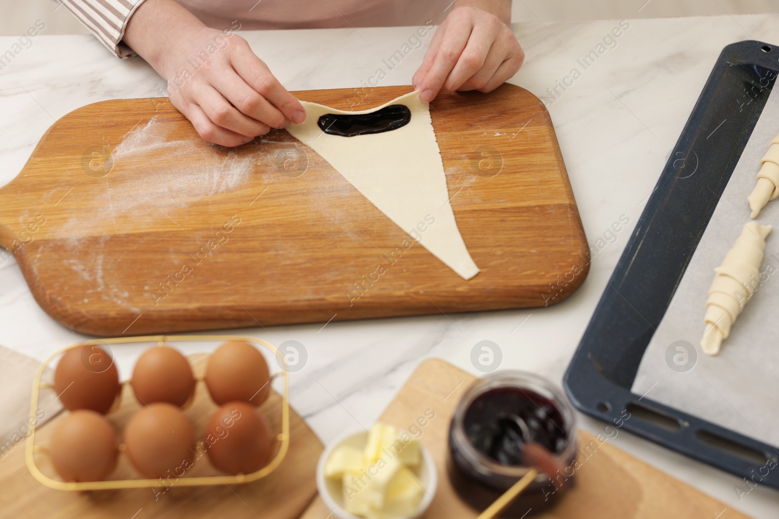 Woman rolling croissant with jam from fresh dough at white marble table, closeup Photo of Woman rolling croissant with jam from fresh dough at white marble table, closeup