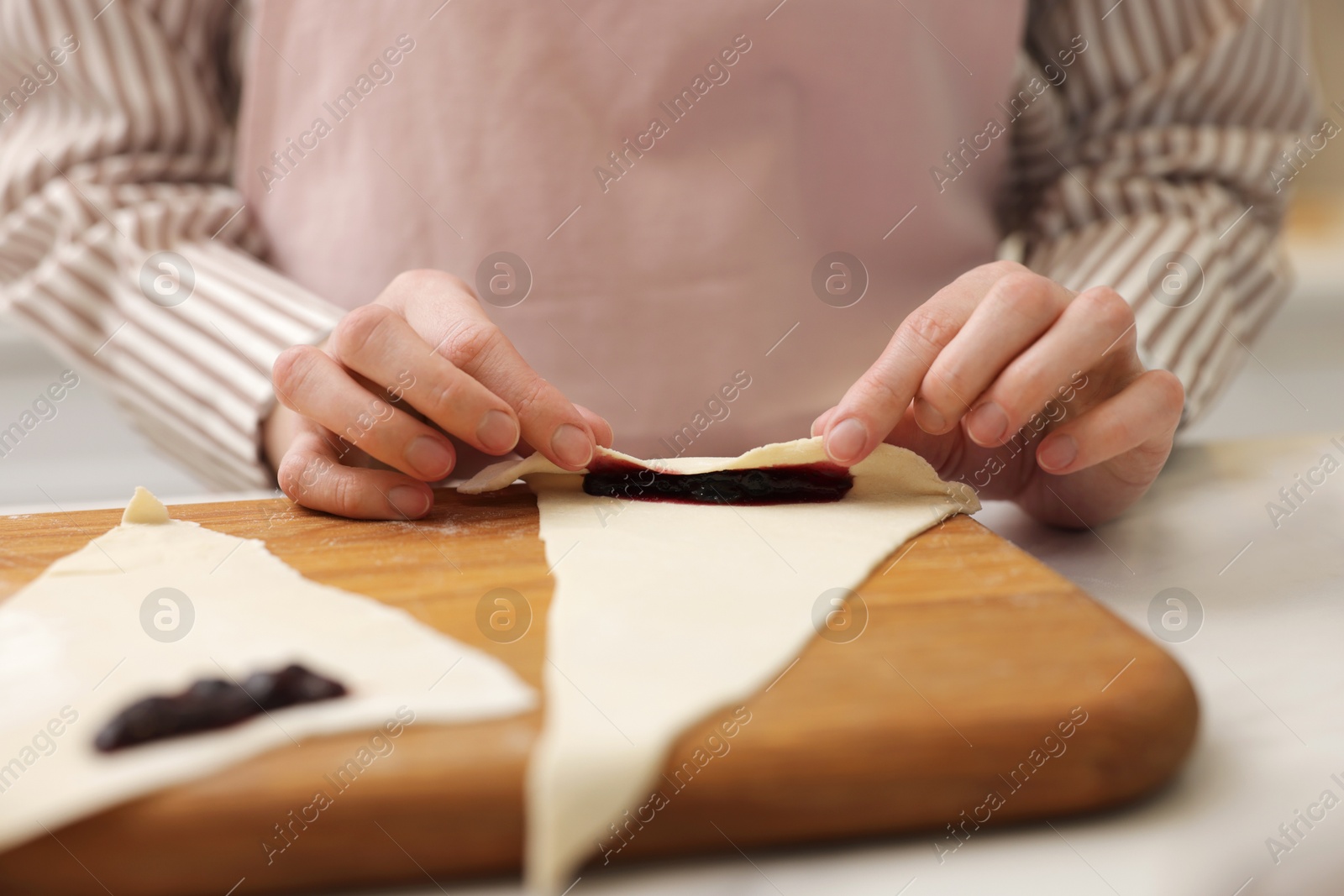 Woman rolling croissant with jam from fresh dough at table, closeup Photo of Woman rolling croissant with jam from fresh dough at table, closeup