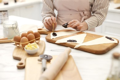 Photo of Woman spreading jam onto fresh dough at white marble table indoors, closeup. Making croissants