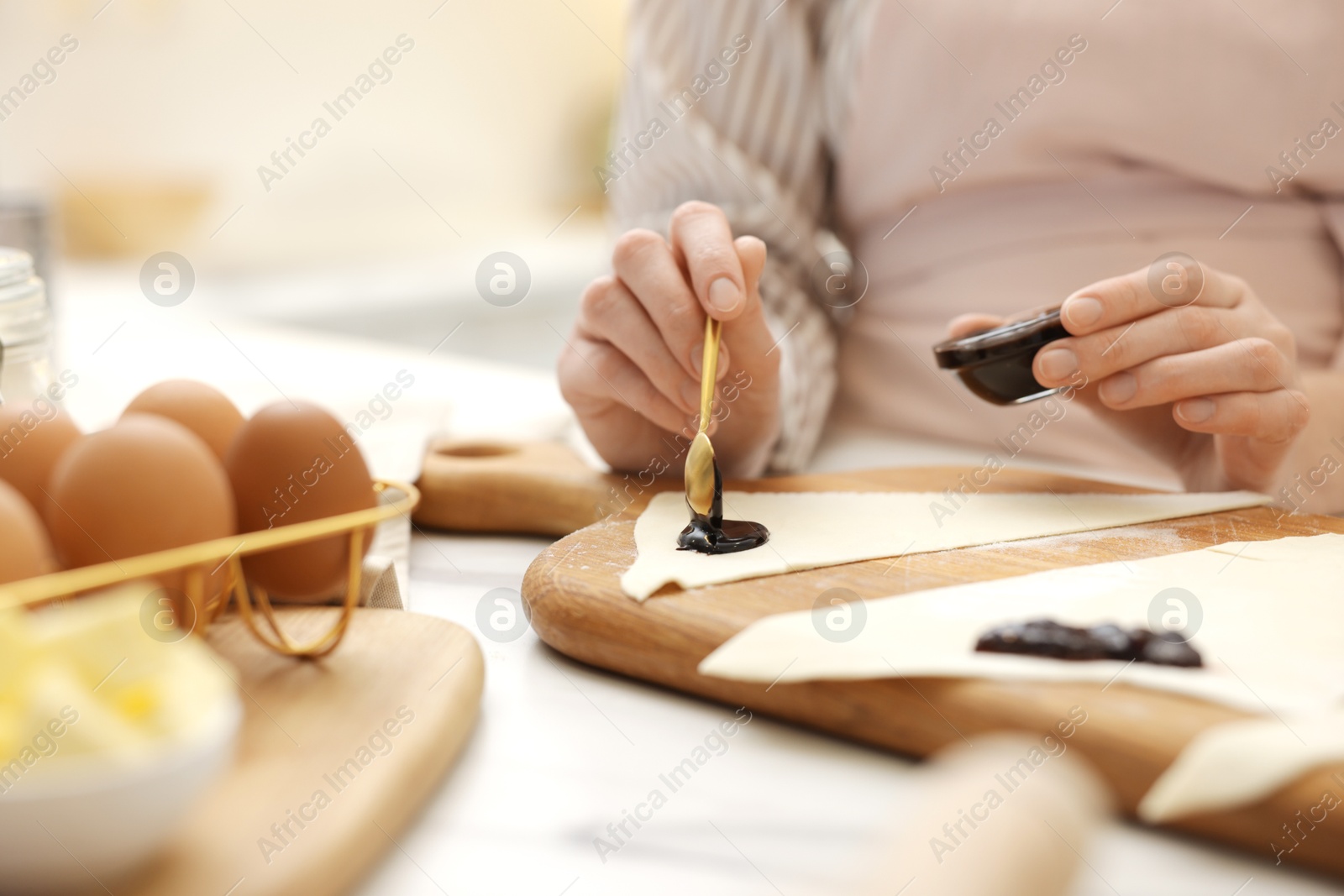 Woman spreading jam onto fresh dough at white table indoors, closeup. Making croissants Photo of Woman spreading jam onto fresh dough at white table indoors, closeup. Making croissants
