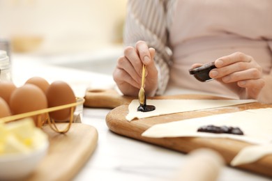 Photo of Woman spreading jam onto fresh dough at white table indoors, closeup. Making croissants