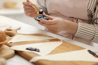 Photo of Woman with jam and fresh dough at white table indoors, closeup. Making croissants