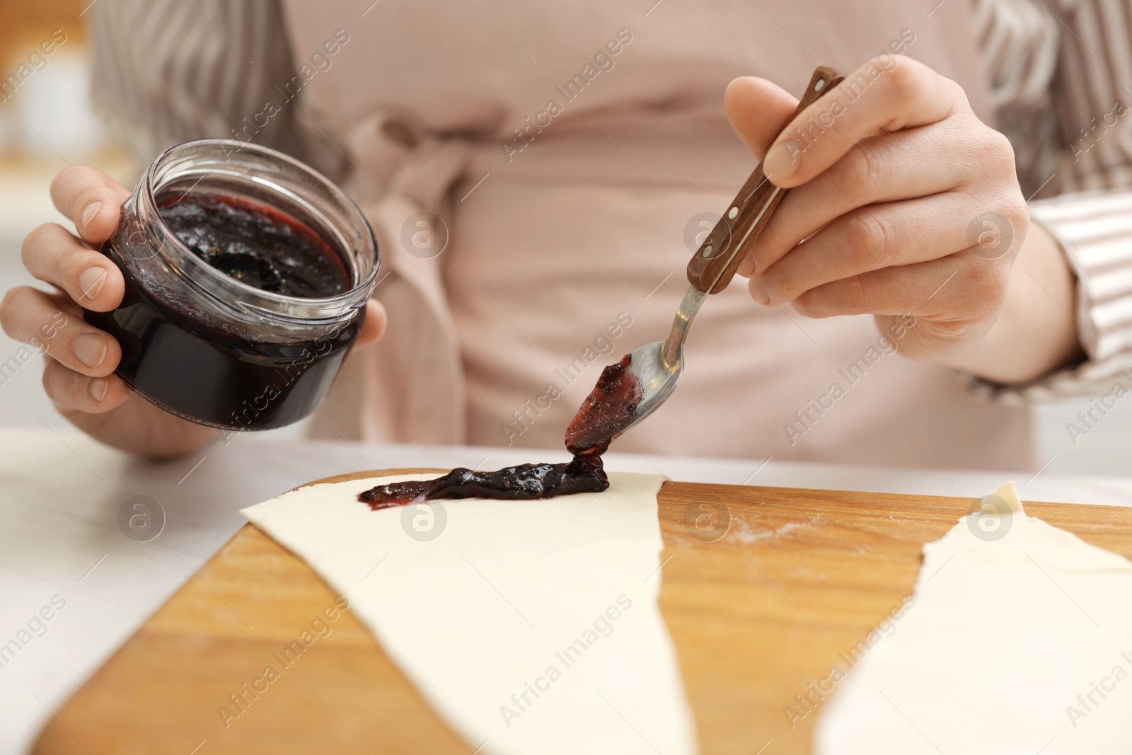Woman spreading jam onto fresh dough at white table, closeup. Making croissants Photo of Woman spreading jam onto fresh dough at white table, closeup. Making croissants