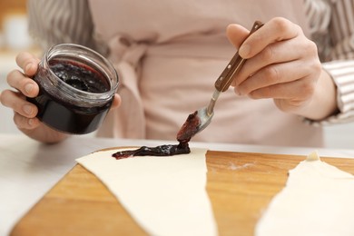 Photo of Woman spreading jam onto fresh dough at white table, closeup. Making croissants