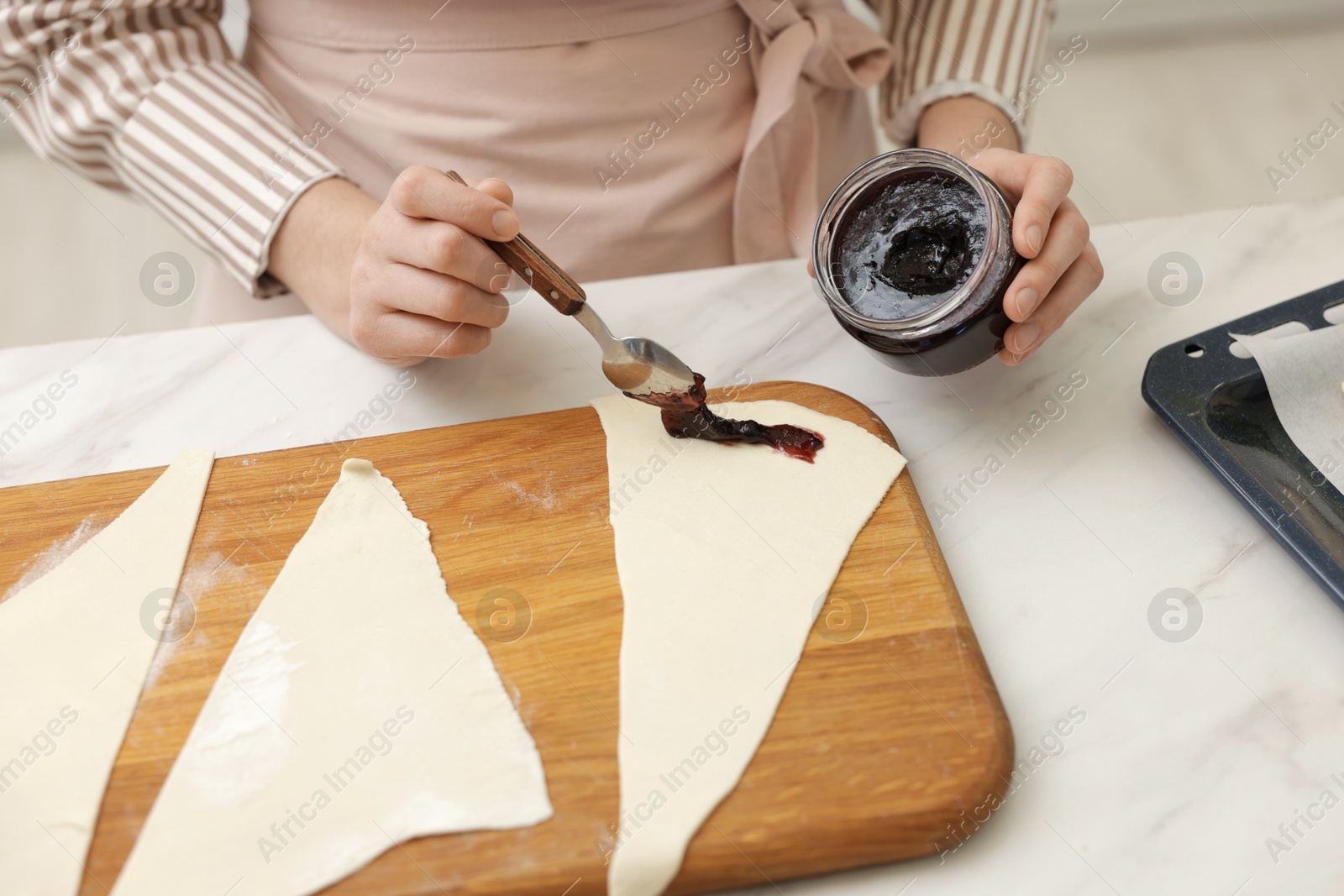 Woman spreading jam onto fresh dough at white marble table indoors, closeup. Making croissants Photo of Woman spreading jam onto fresh dough at white marble table indoors, closeup. Making croissants