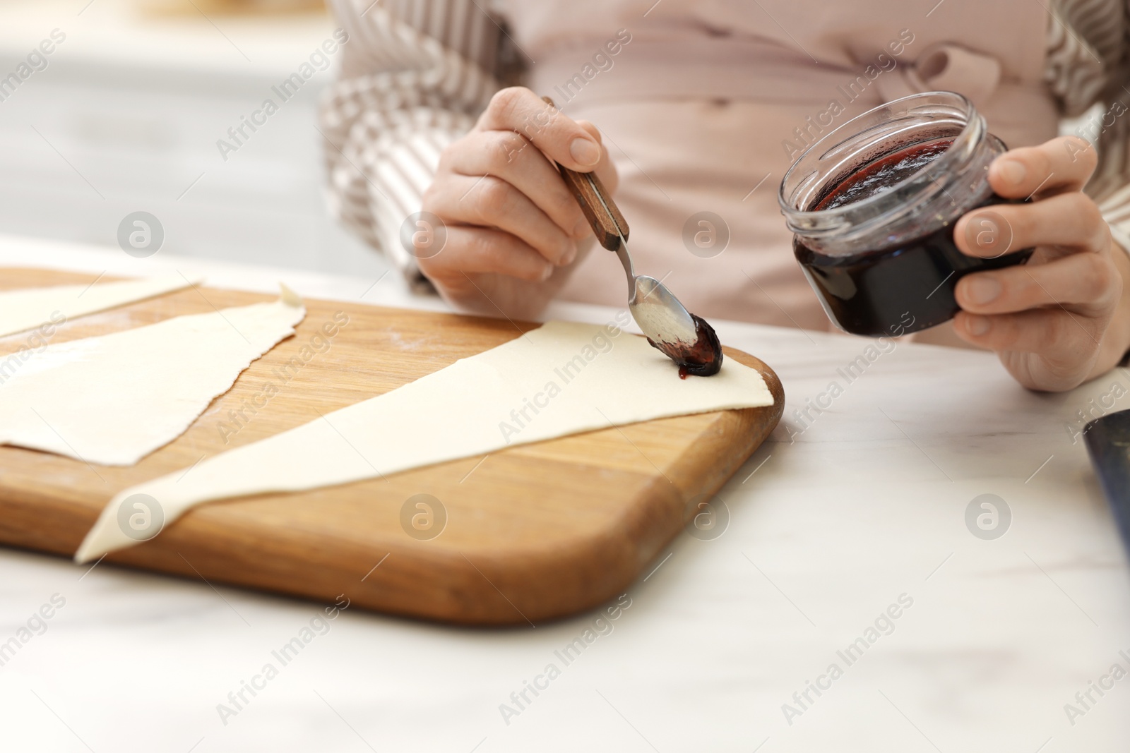 Woman spreading jam onto fresh dough at white marble table indoors, closeup. Making croissants Photo of Woman spreading jam onto fresh dough at white marble table indoors, closeup. Making croissants