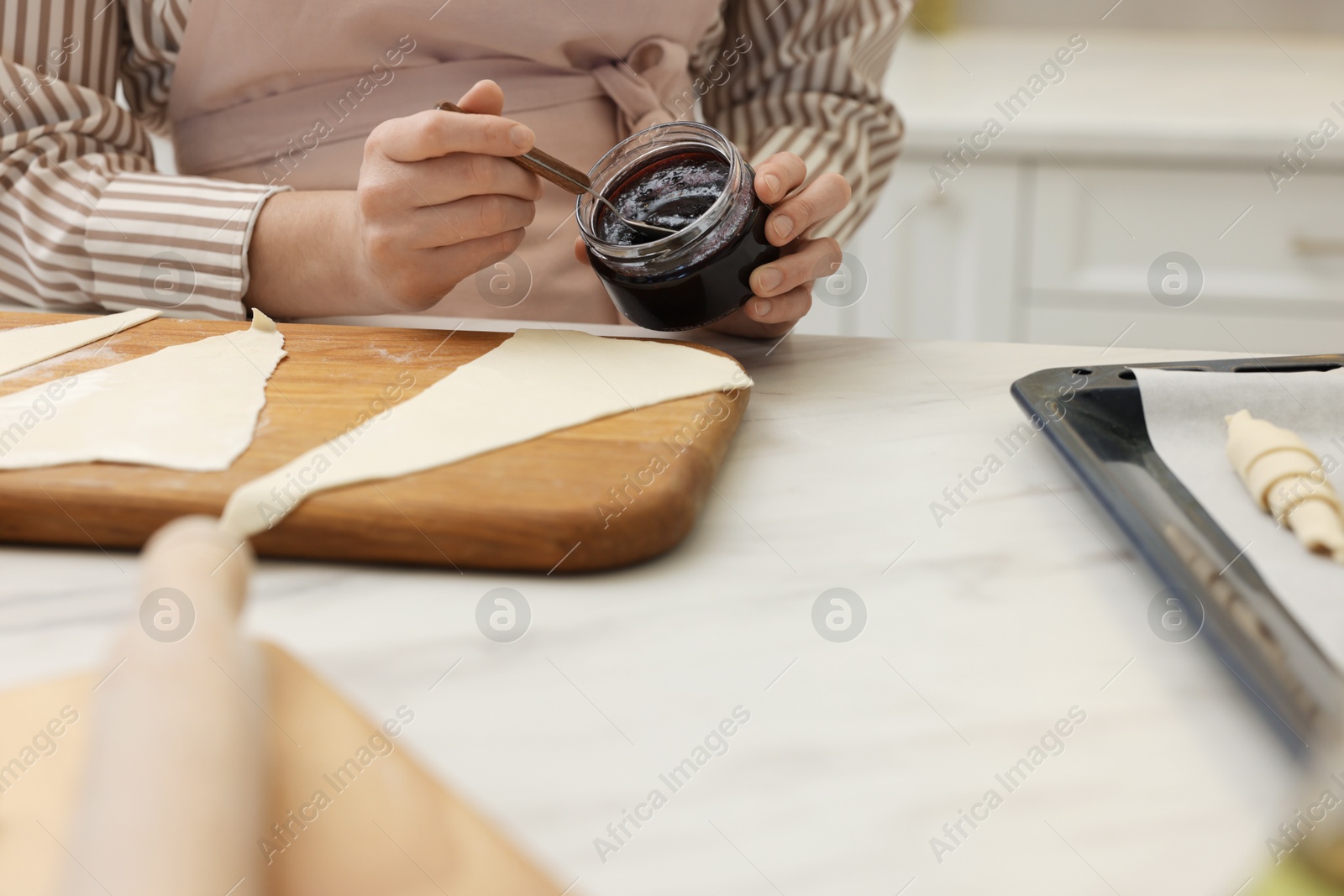 Woman spreading jam onto fresh dough at white marble table indoors, closeup. Making croissants Photo of Woman spreading jam onto fresh dough at white marble table indoors, closeup. Making croissants