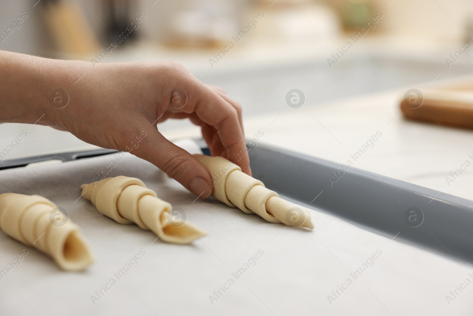 Woman putting raw croissants onto baking sheet at white table indoors, closeup Photo of Woman putting raw croissants onto baking sheet at white table indoors, closeup