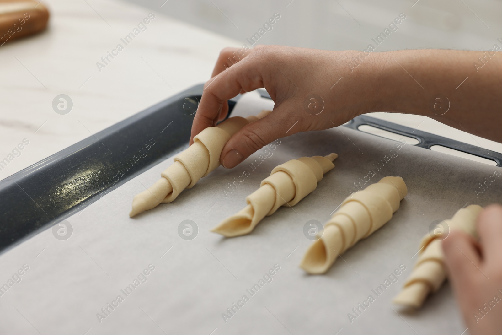 Woman putting raw croissants onto baking sheet at white table indoors, closeup Photo of Woman putting raw croissants onto baking sheet at white table indoors, closeup