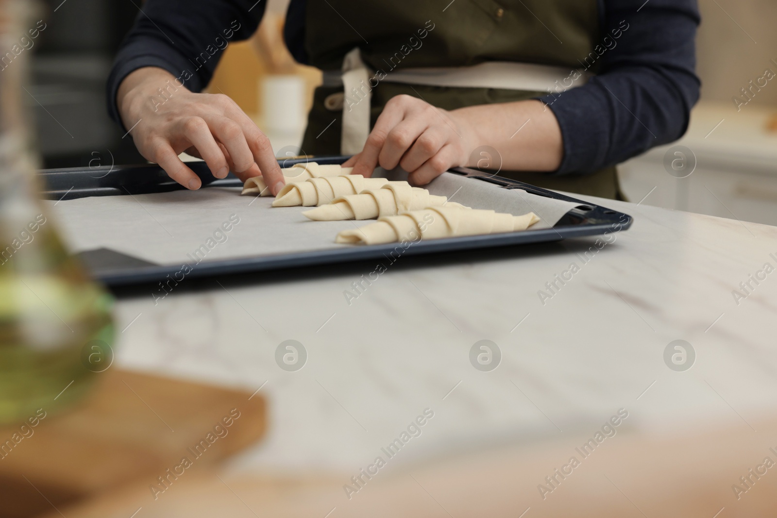 Woman putting raw croissants onto baking sheet at white table indoors, closeup Photo of Woman putting raw croissants onto baking sheet at white table indoors, closeup
