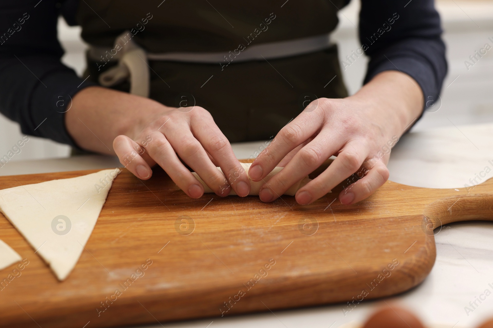 Woman rolling croissant from fresh dough at light table, closeup Photo of Woman rolling croissant from fresh dough at light table, closeup