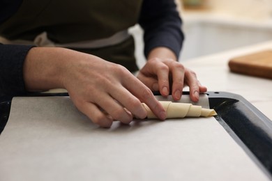 Photo of Woman putting raw croissant onto baking sheet at light table indoors, closeup