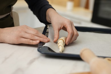 Photo of Woman putting raw croissant onto baking sheet at white marble table indoors, closeup