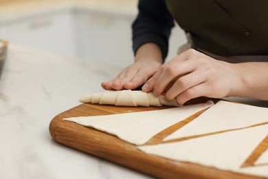 Photo of Woman making croissant at light marble table indoors, closeup