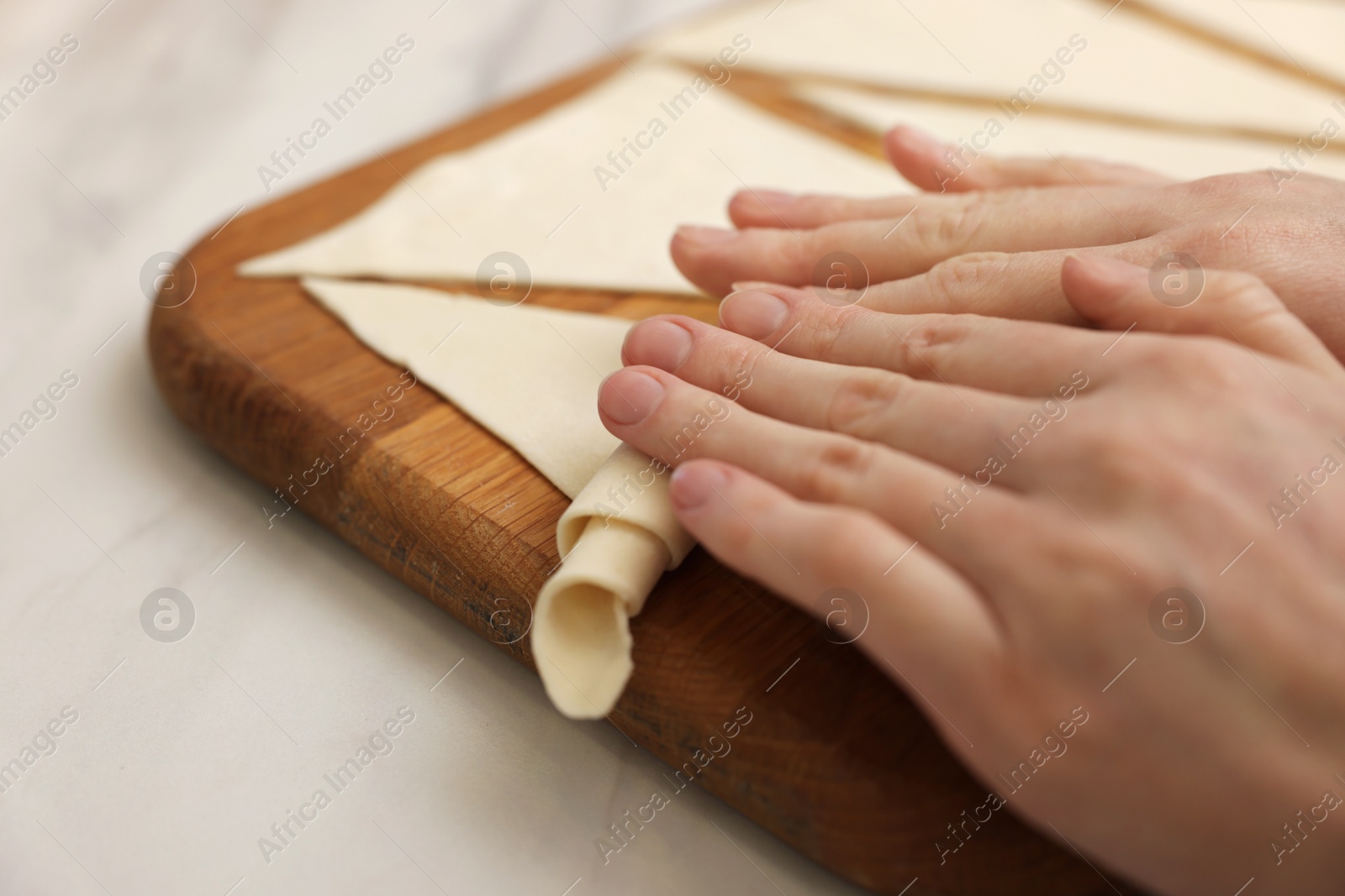 Woman rolling croissant from fresh dough at light table, closeup Photo of Woman rolling croissant from fresh dough at light table, closeup