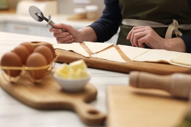 Photo of Woman with dough cutter and ingredients at light table indoors, selective focus. Making croissants