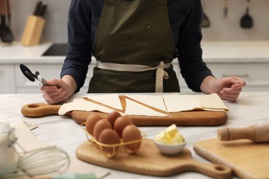 Woman with dough cutter and ingredients at light marble table indoors, selective focus. Making croissants