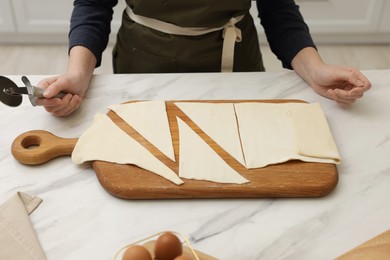 Photo of Woman with dough and cutter at light marble table indoors, closeup. Making croissants