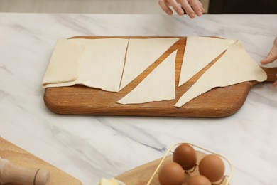 Photo of Woman with cut dough at light marble table indoors, closeup. Making croissants