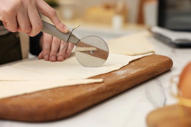 Photo of Woman cutting dough at light marble table indoors, closeup. Making croissants