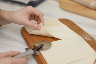 Photo of Woman cutting dough at light table, closeup. Making croissants