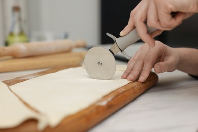 Photo of Woman cutting dough at light table, closeup. Making croissants