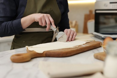 Photo of Woman cutting dough at light marble table indoors, closeup. Making croissants