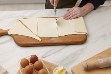 Photo of Woman cutting dough at light marble table, closeup. Making croissants