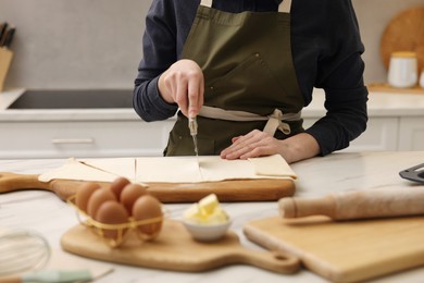 Photo of Woman cutting dough at light marble table indoors, closeup. Making croissants