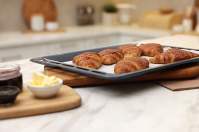 Photo of Freshly baked croissants, butter and jam on white marble table indoors, selective focus