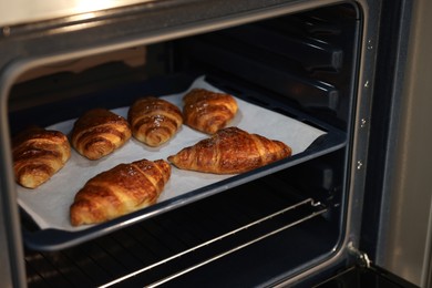 Photo of Freshly baked croissants on baking sheet in oven, closeup