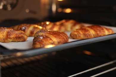 Photo of Freshly baked croissants on baking sheet in oven, closeup