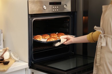 Photo of Woman taking baking sheet with tasty croissants out of oven indoors, closeup