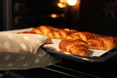 Photo of Woman taking baking sheet with tasty croissants out of oven, closeup