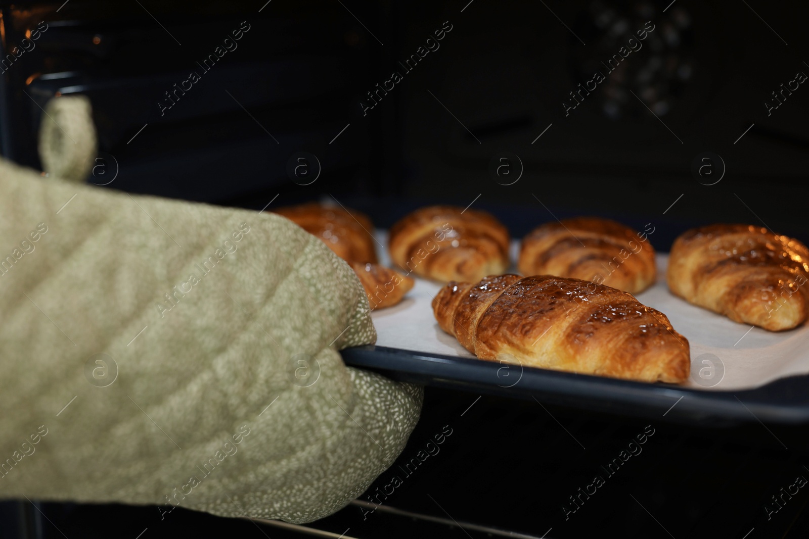 Woman taking baking sheet with tasty croissants out of oven, closeup Photo of Woman taking baking sheet with tasty croissants out of oven, closeup