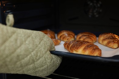 Photo of Woman taking baking sheet with tasty croissants out of oven, closeup