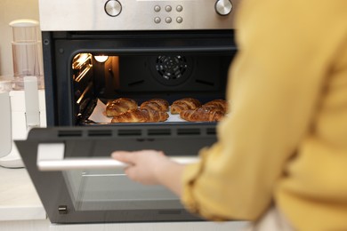 Photo of Woman opening oven with tasty croissants indoors, closeup