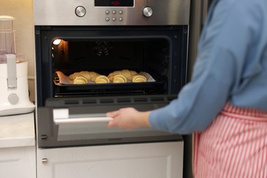 Photo of Woman closing oven with raw croissants indoors, closeup