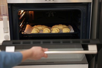 Photo of Woman closing oven with raw croissants, closeup