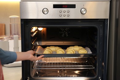 Photo of Woman putting baking sheet with raw croissants into oven indoors, closeup