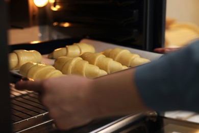 Woman putting baking sheet with raw croissants into oven, selective focus